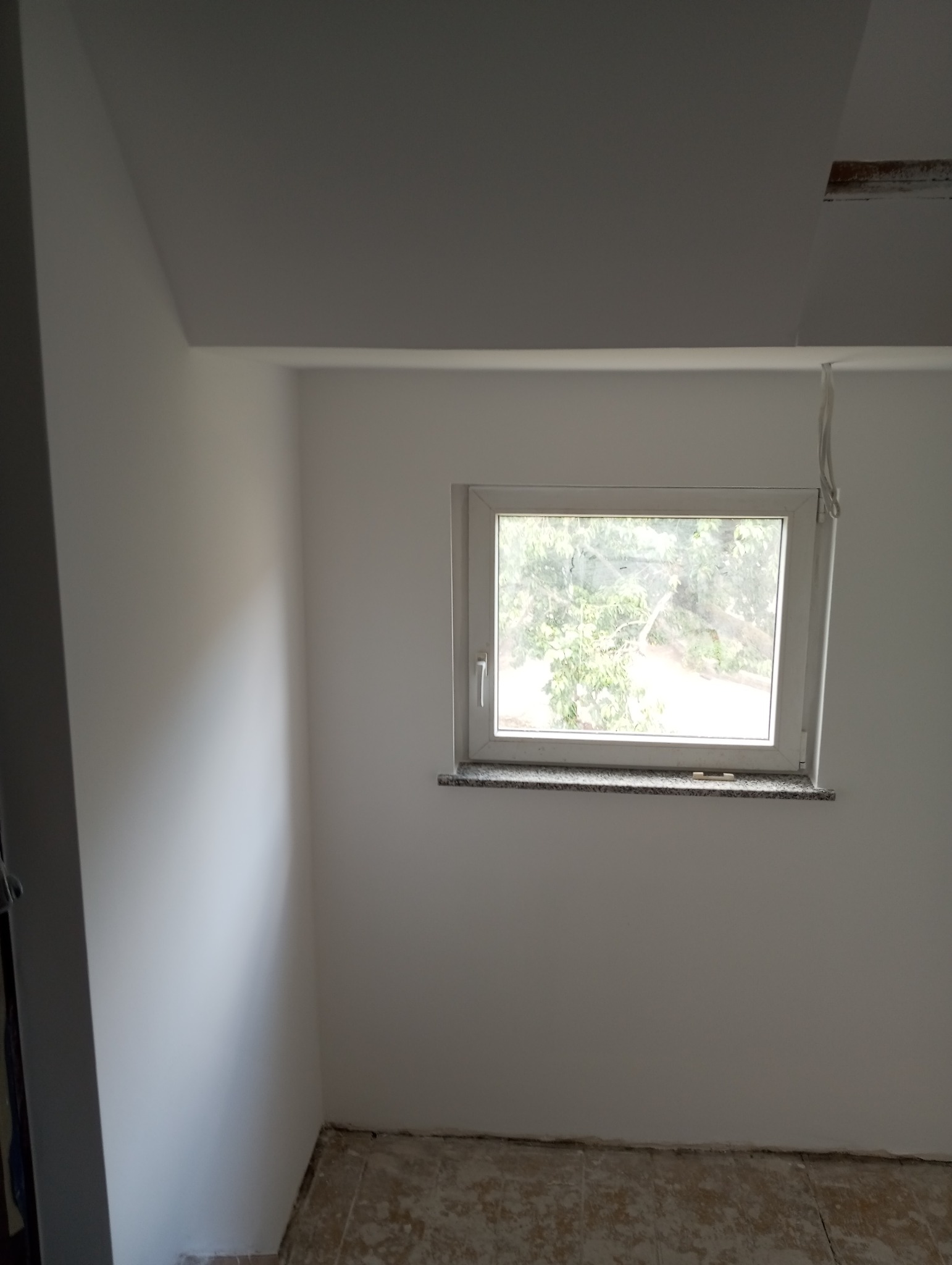 Świeżo pomalowane na biało wnętrze pokoju z oknem, widoczne niedoskonałości na podłodze przed ostatecznym wykończeniem.