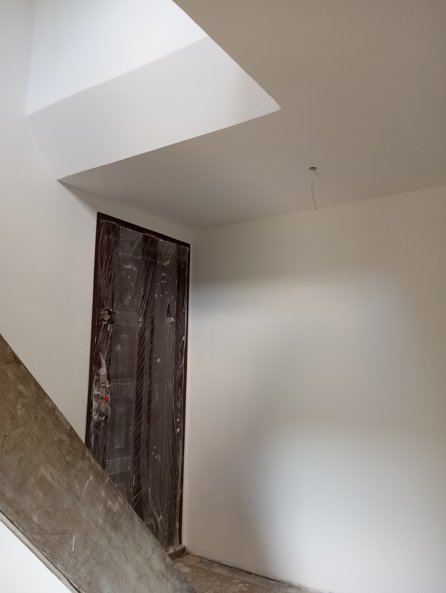 Wnętrze w trakcie malowania, zabezpieczone drzwi folią ochronną, widoczny fragment schodów i pomalowane ściany na biało.