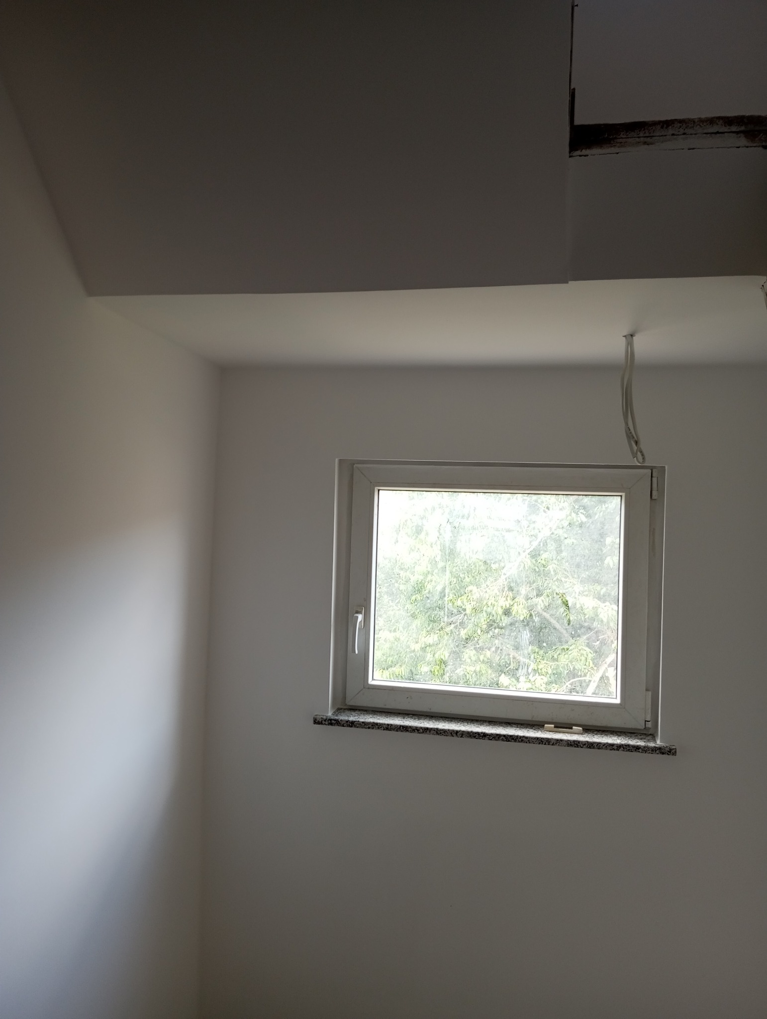 Wnętrze pokoju po świeżym malowaniu ścian na biało w Bolesławcu, widoczne okno z kamiennym parapetem i wystające przewody elektryczne z sufitu.