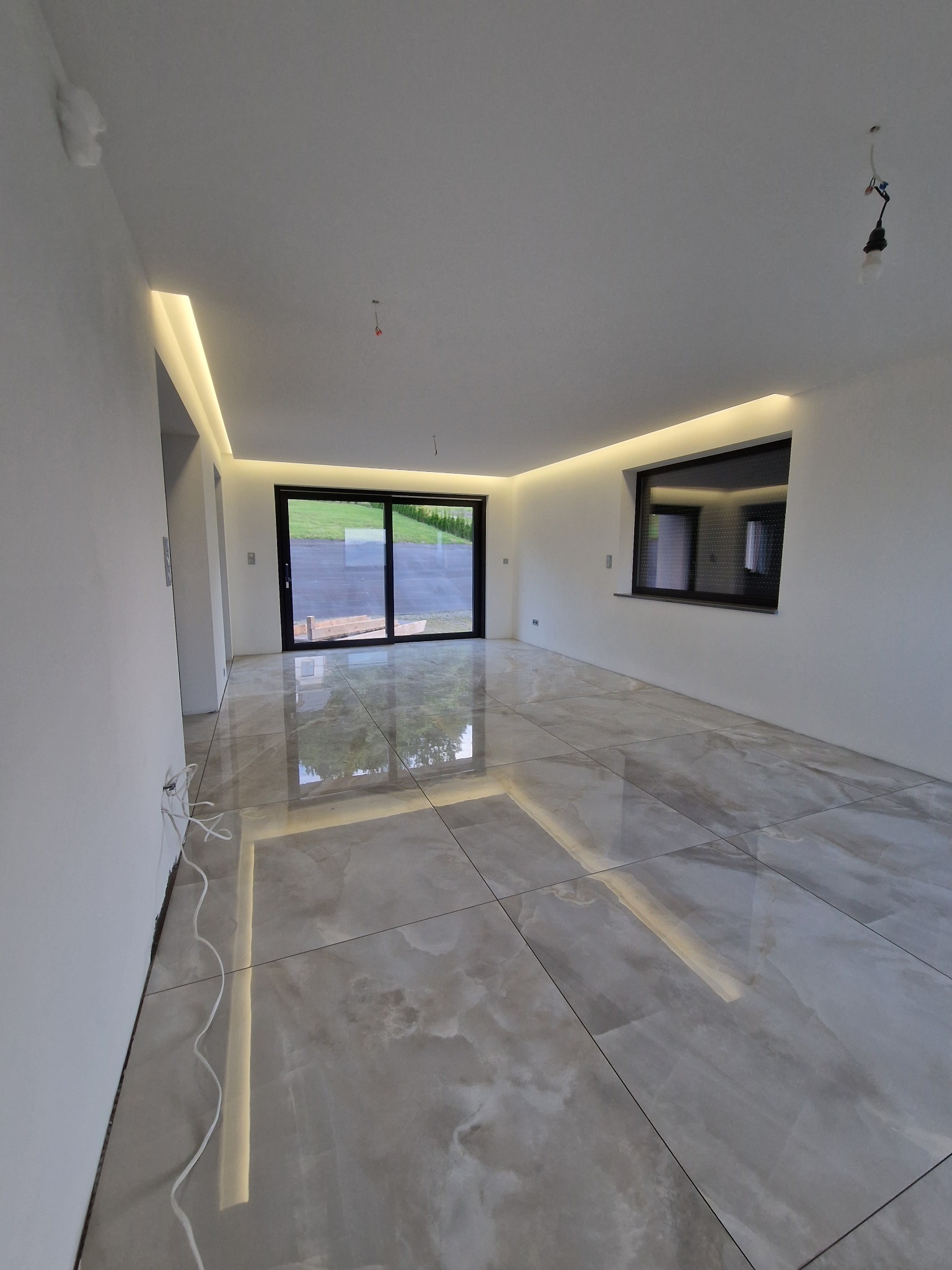 Wykończone wnętrze z marmurową podłogą, oświetleniem LED wzdłuż sufitu i ścian, oraz widokiem na zewnątrz przez duże przesuwne okno.