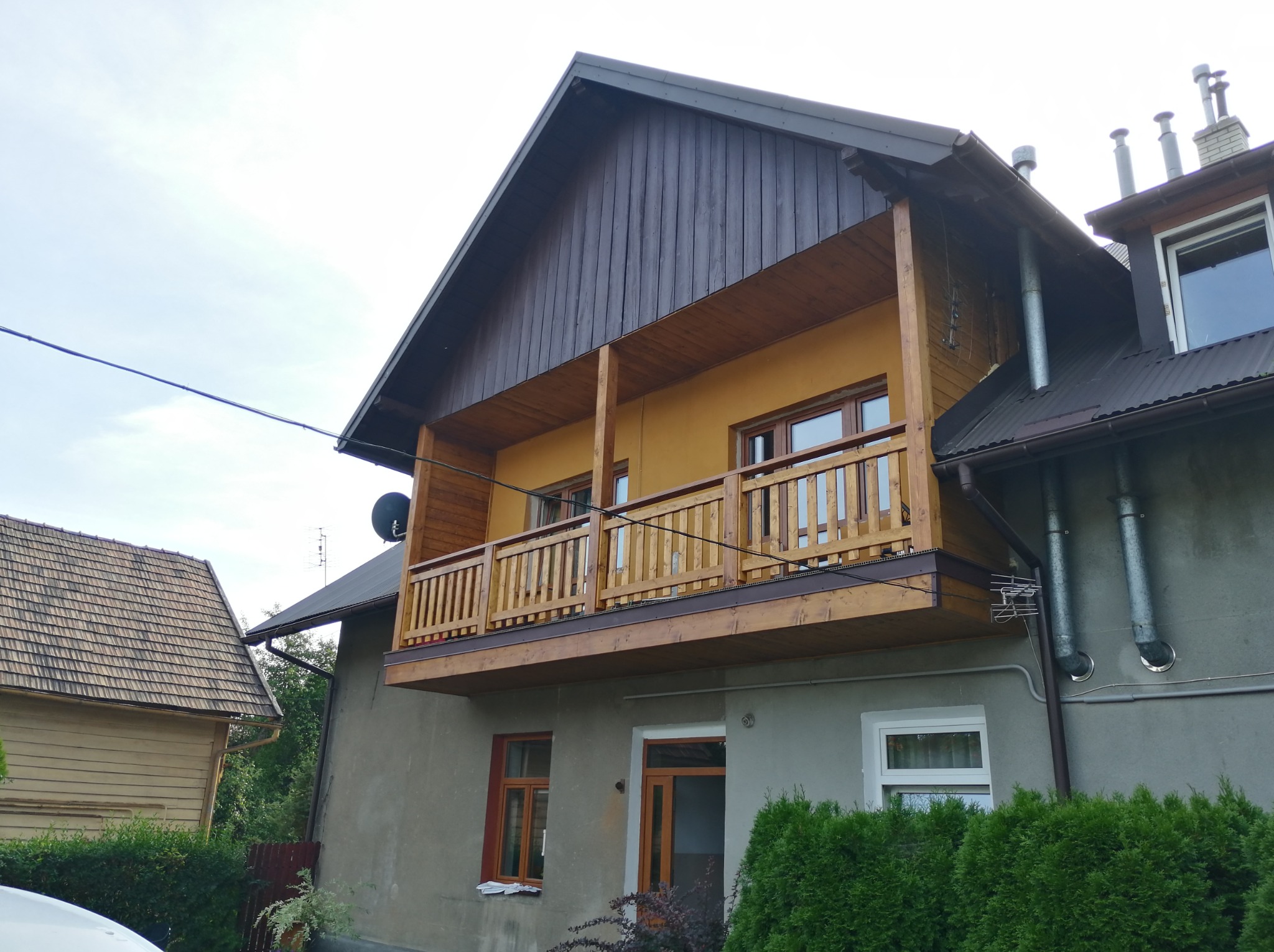 Dwukondygnacyjny dom z drewnianym balkonem wspartym na słupach, widoczne rynny, antena satelitarna i kominy