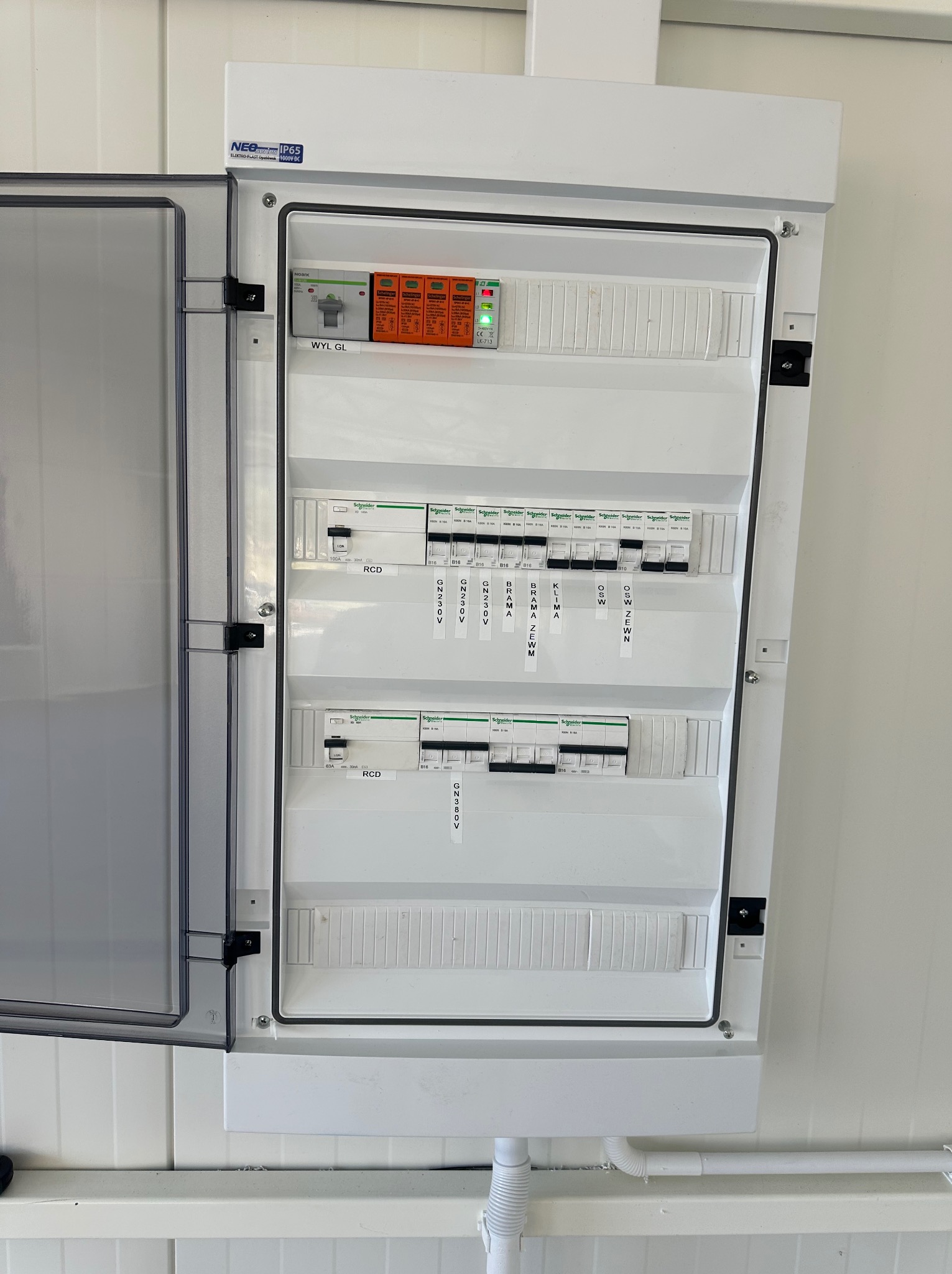 Otwarta skrzynka elektryczna z bezpiecznikami i wyłącznikami różnicowoprądowymi Schneider Electric, etykiety opisujące obwody: Brama, Klima, Oświetlenie Zewnętrzne, Gniazda 230V i 380V.