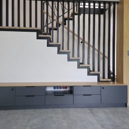 Meble w Twojej okolicy - Nowoczesne schody z czarną balustradą i drewnianymi stopniami, zintegrowane z szarą szafką na ścianie. Widoczne gniazdka elektryczne. Minimalistyczny design.