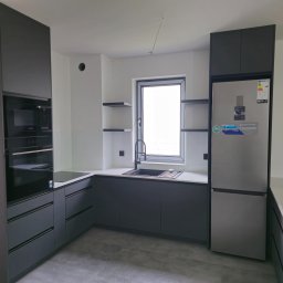 Meble w Twojej okolicy - Nowoczesna kuchnia w odcieniach szarości z białym blatem i srebrną lodówką. Minimalistyczny design z otwartymi półkami i zabudowanym sprzętem AGD.