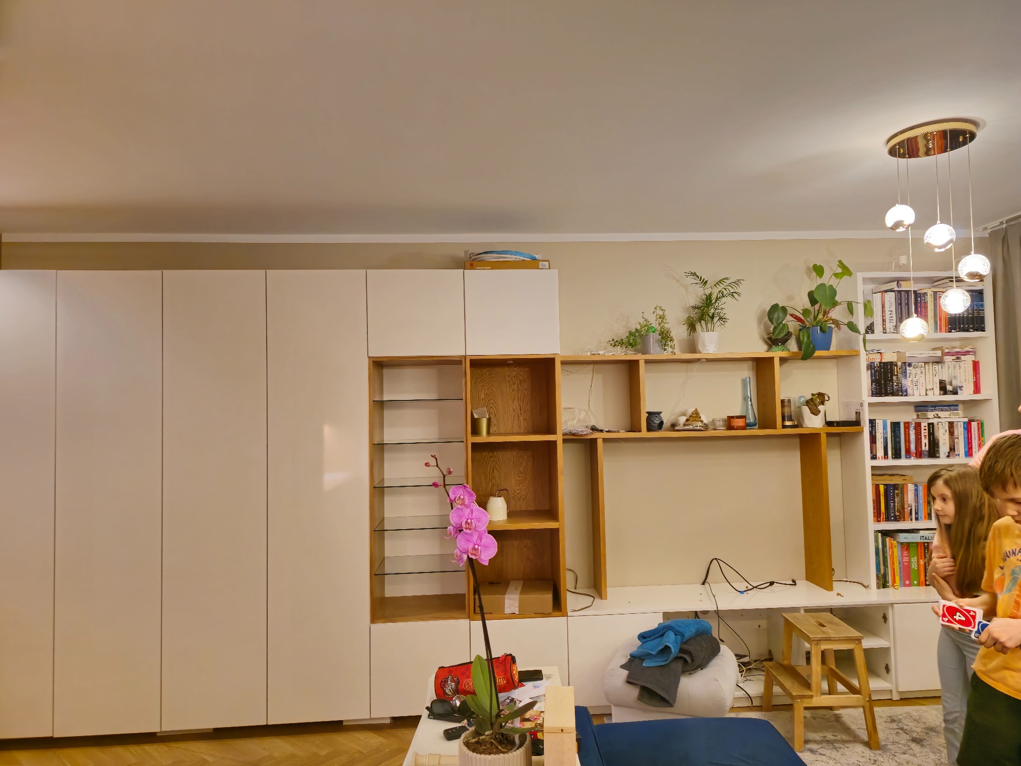 Biała zabudowa meblowa z półkami i szafkami w salonie w Ulan-Majorat. Na pierwszym planie kwiat orchidei. Na półkach książki i dekoracje.