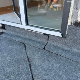 Jakub Markuszewski - Pęknięcia na papie dachowej przy oknie dachowym. Widoczne uszkodzenia i nieszczelności warstwy hydroizolacyjnej dachu płaskiego.