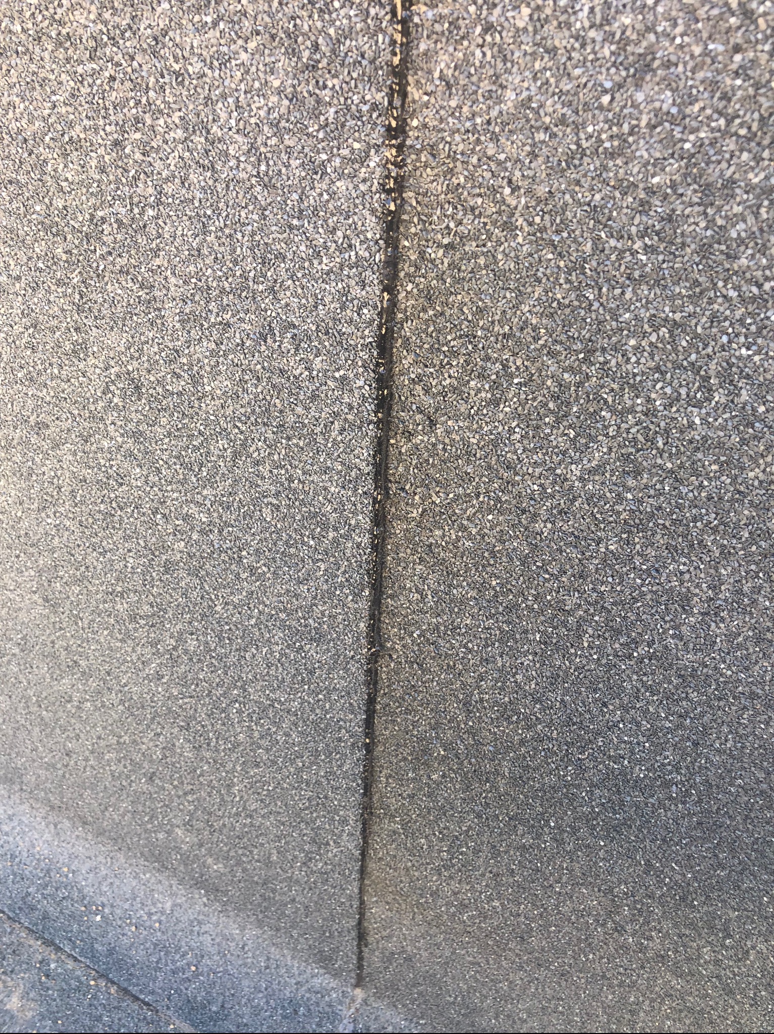 Zbliżenie na szary, bitumiczny gont dachowy z widoczną linią łączenia. Tekstura z drobnymi kamyczkami.