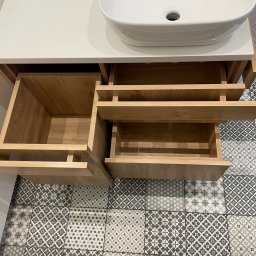 LookMeble - Szafka łazienkowa z umywalką i otwartymi szufladami z jasnego drewna na tle wzorzystej podłogi w szarościach. Widok z góry.