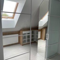 LookMeble - Szafa wnękowa z przesuwnymi drzwiami z mlecznego szkła i lustra w jasnym pokoju na poddaszu z oknem dachowym. Widoczne półki wewnątrz szafy.