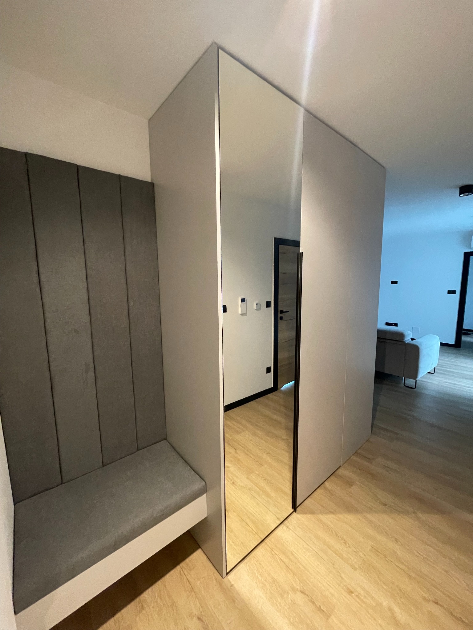 Nowoczesna szafa wnękowa z lustrem i tapicerowanym siedziskiem w przedpokoju, Nowy Sącz. Minimalistyczny design, jasne kolory i funkcjonalne rozwiązanie do przechowywania.