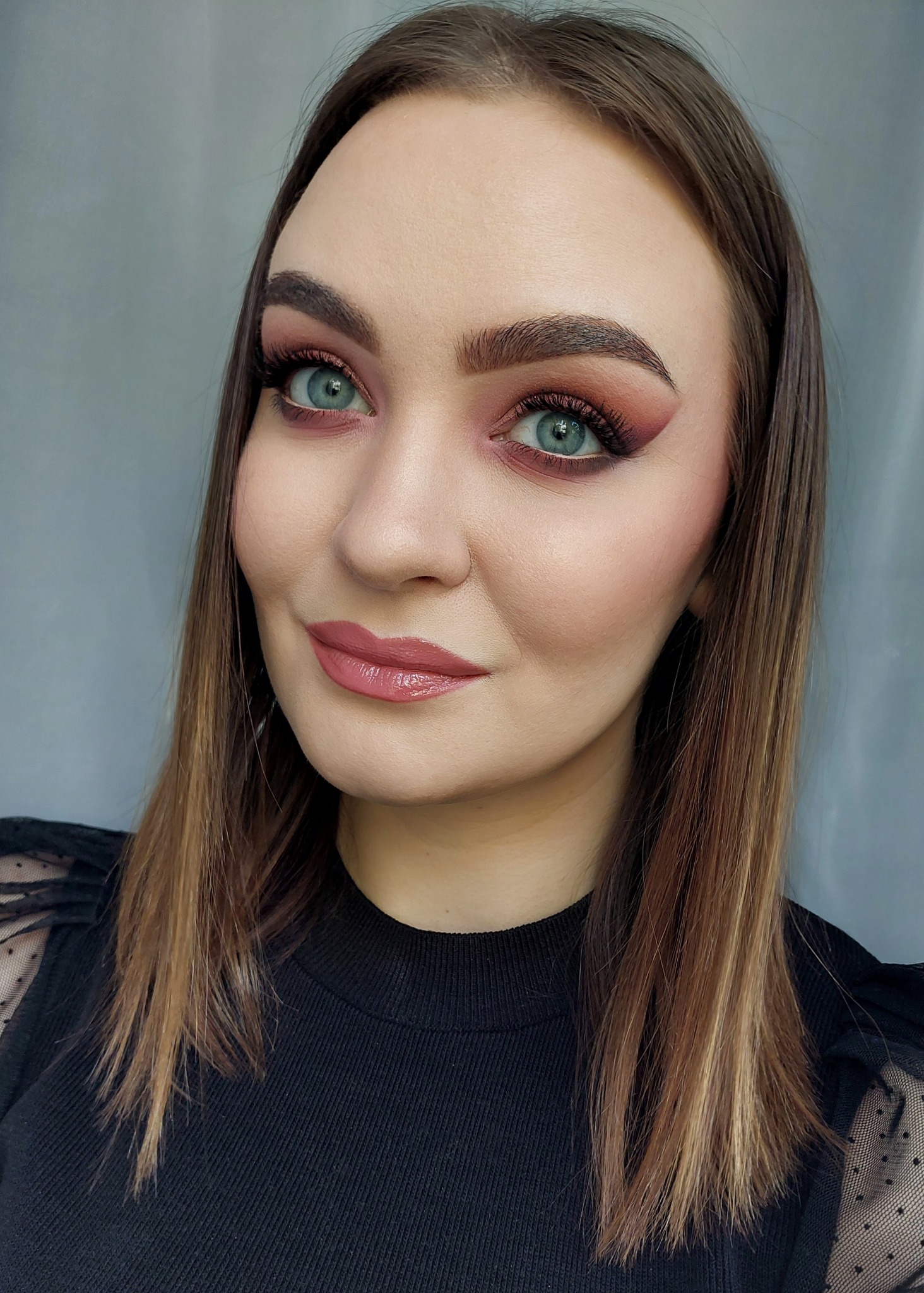 Portret kobiety z subtelnym, różowo-brązowym cieniowaniem powiek i błyszczącymi ustami w odcieniu nude, włosy ombre.