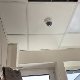 LightTech Oleksandr Liutyi - Kamera monitoringu kopułkowa zamontowana na suficie podwieszanym w biurze w Warszawie, widoczne kable i puszki instalacyjne w przestrzeni nad sufitem.