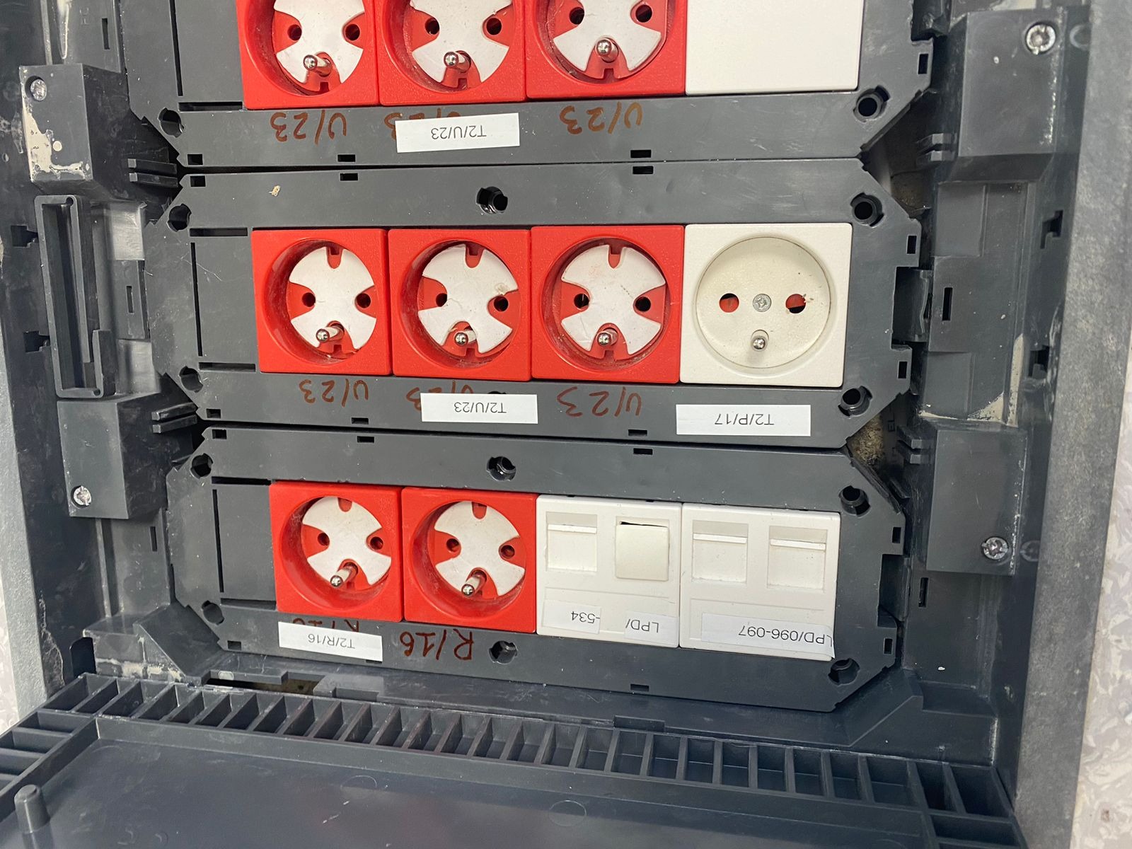 Rozdzielnica elektryczna z gniazdkami przemysłowymi w kolorze czerwonym i białym, widoczne etykiety z datami przeglądów.
