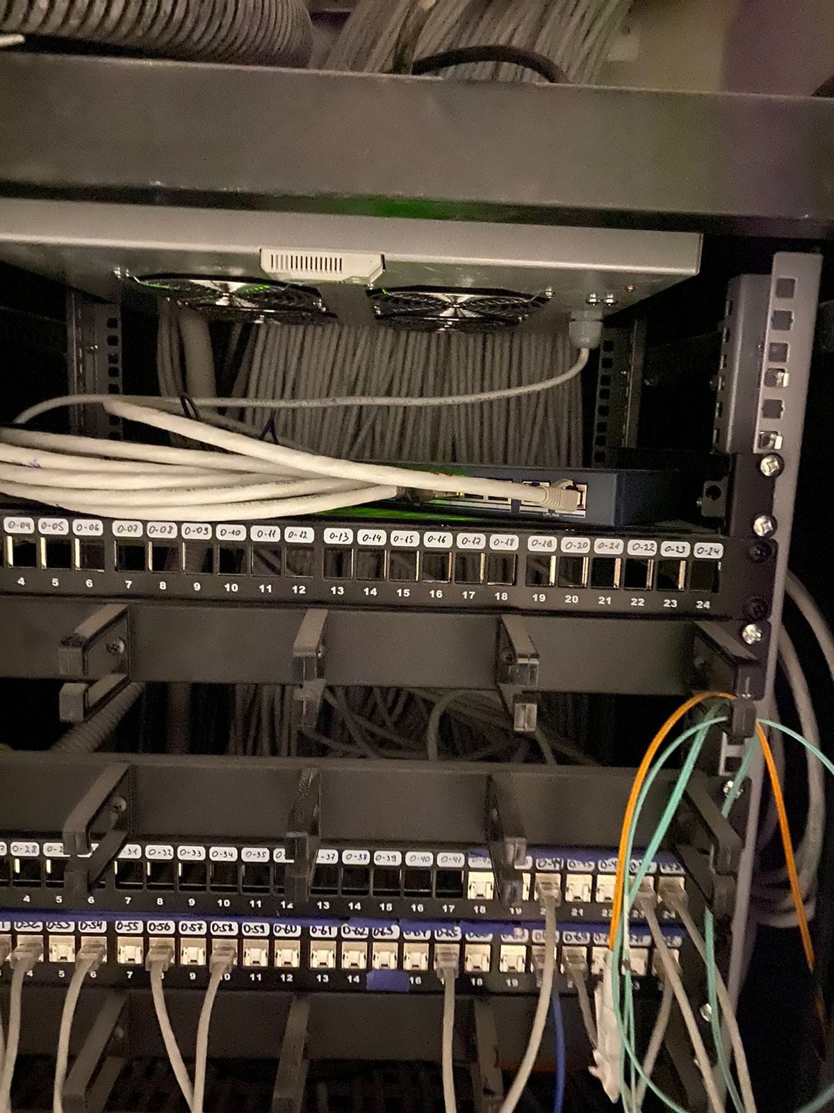 Panel krosowniczy z podłączonymi kablami sieciowymi w szafie rack, widoczne oznaczenia portów i wentylatory chłodzące