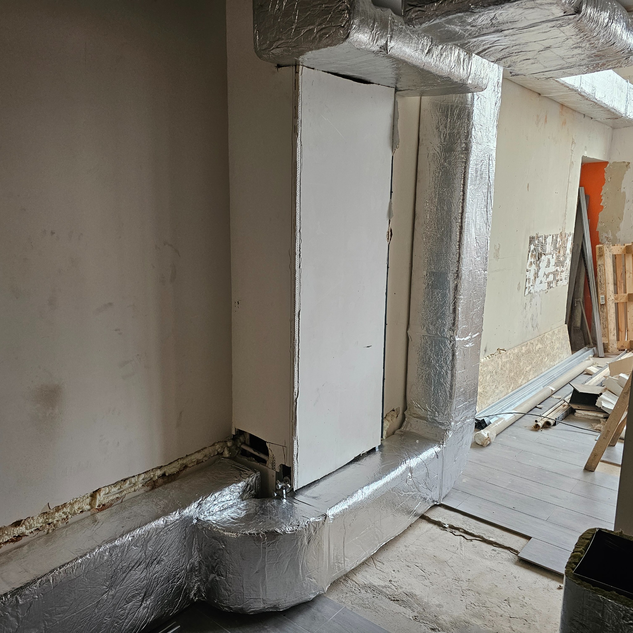 Izolowane folią aluminiową kanały wentylacyjne w trakcie montażu w surowym wnętrzu. Widoczne niedokończone ściany, podłoga i elementy konstrukcyjne.