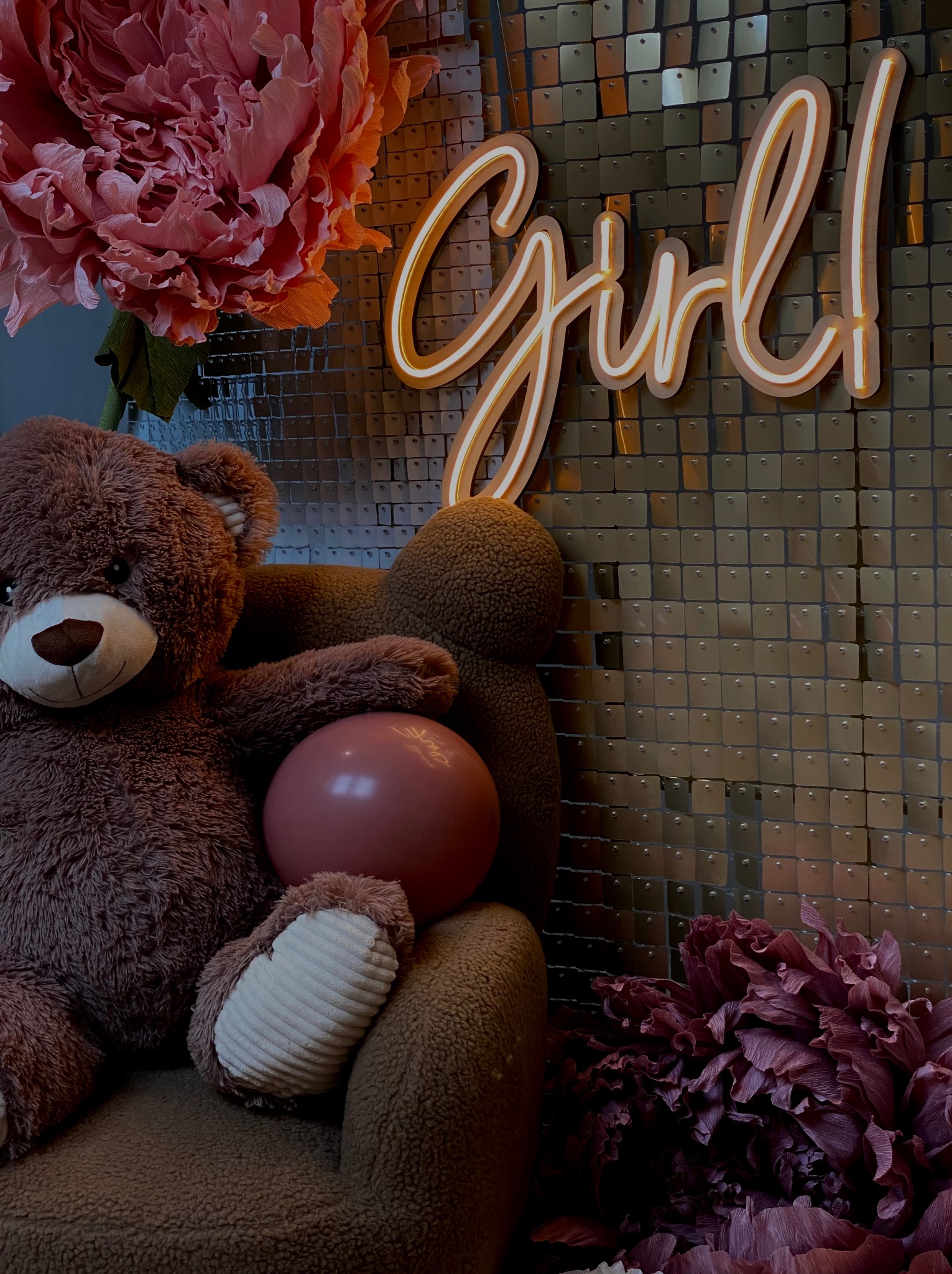 Dekoracja na baby shower dla dziewczynki: pluszowy miś z różowym balonem, neon 'Girl!', tło z cekinów i papierowe kwiaty.