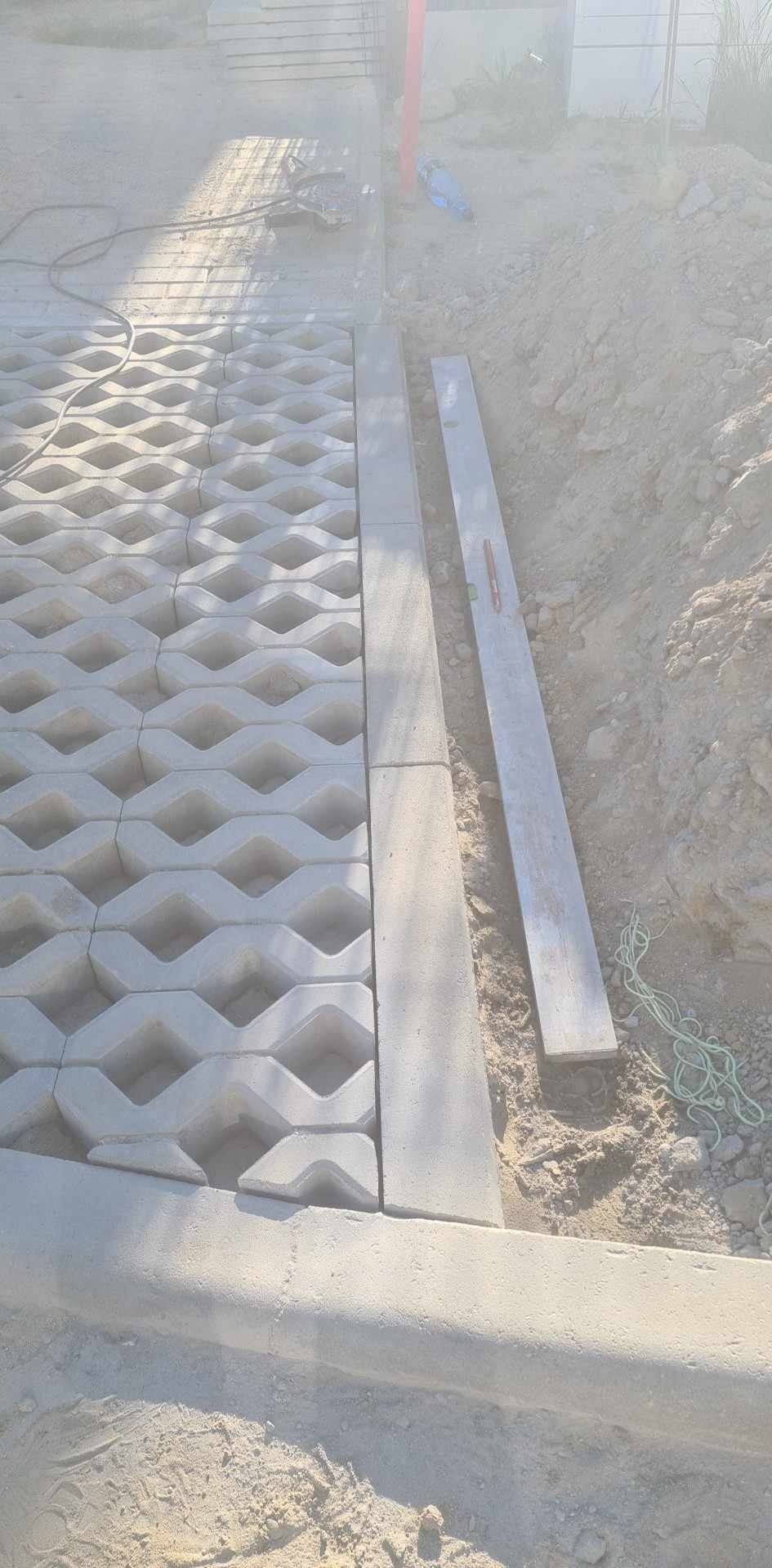 Ułożona ażurowa kostka brukowa z betonowym obrzeżem, widoczne narzędzia i teren przygotowany pod dalsze prace.