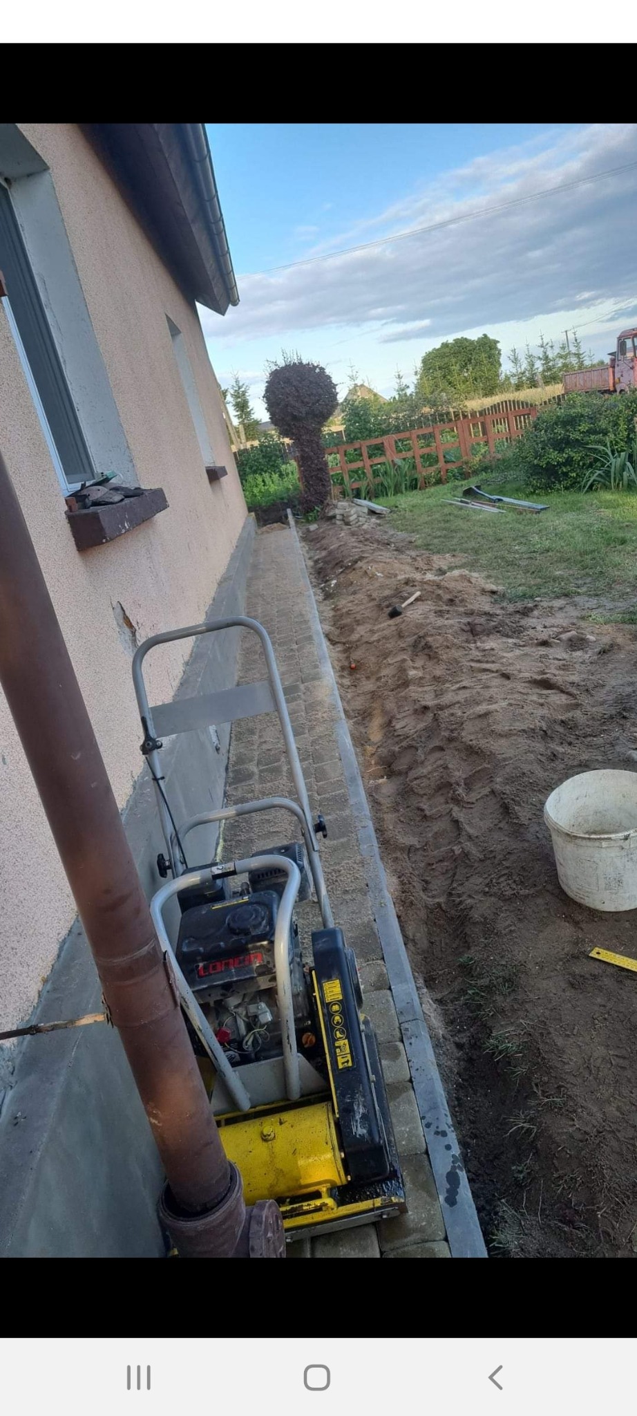 Żółta zagęszczarka obok ułożonej kostki brukowej przy ścianie budynku, w tle przygotowany teren pod dalsze prace.