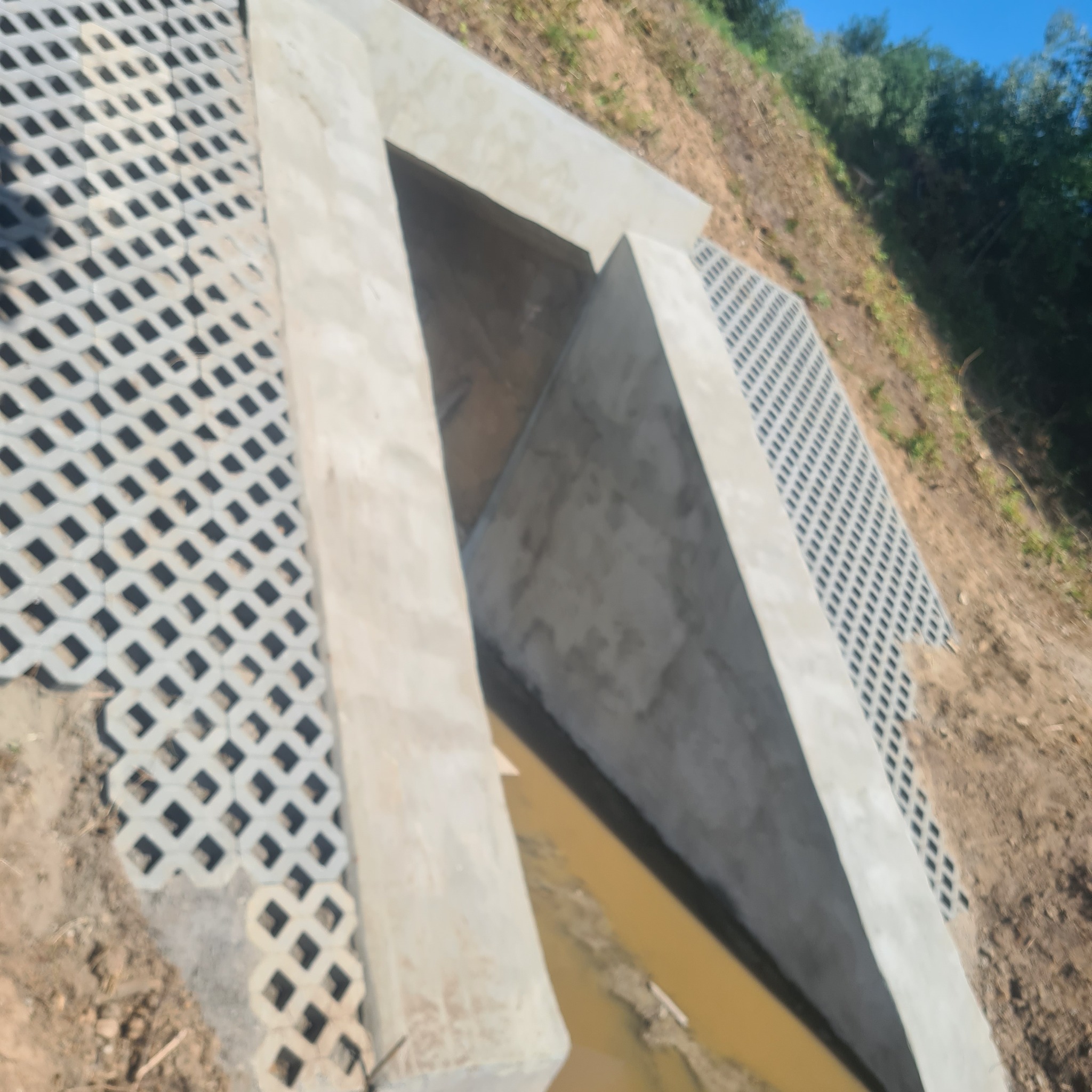 Betonowy przepust odwadniający z ażurowymi płytami na zboczu, odprowadzający wodę gruntową.