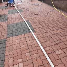 cleanup Karolina Ogrodnik - Profesjonalna myjka ciśnieniowa Kärcher podłączona wężem do kostki brukowej w kolorze czerwono-szarym, przygotowana do czyszczenia na posesji przed ogrodzeniem.