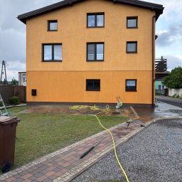 cleanup Karolina Ogrodnik - Dwupiętrowy dom z żółtą elewacją po myciu, z widocznym wężem i mokrym terenem wokół. Ślady wody na elewacji i chodniku.