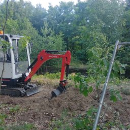 M&K usługi ziemne - Mała koparka Kubota KX3-3 na placu budowy, widoczna świeżo wykopana ziemia i tymczasowe ogrodzenie z siatki, w tle zieleń drzew.