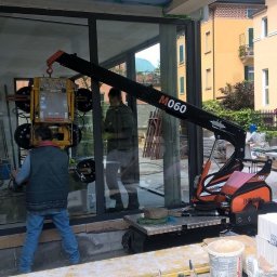 GLASSLIFT Katarzyna Motyczyńska - Montaż okna za pomocą mini żurawia ssącego M060 w Zgierzu, widoczne budynki w tle i pracownicy budowlani.