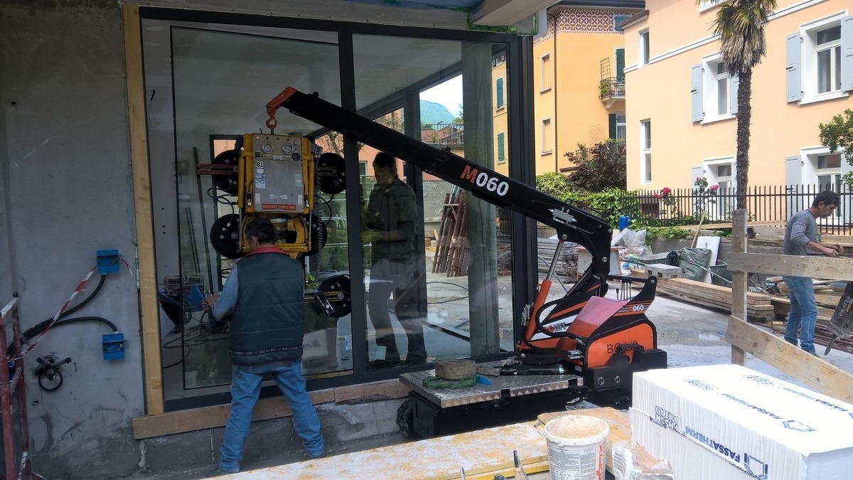 Montaż okna za pomocą mini żurawia ssącego M060 w Zgierzu, widoczne budynki w tle i pracownicy budowlani.