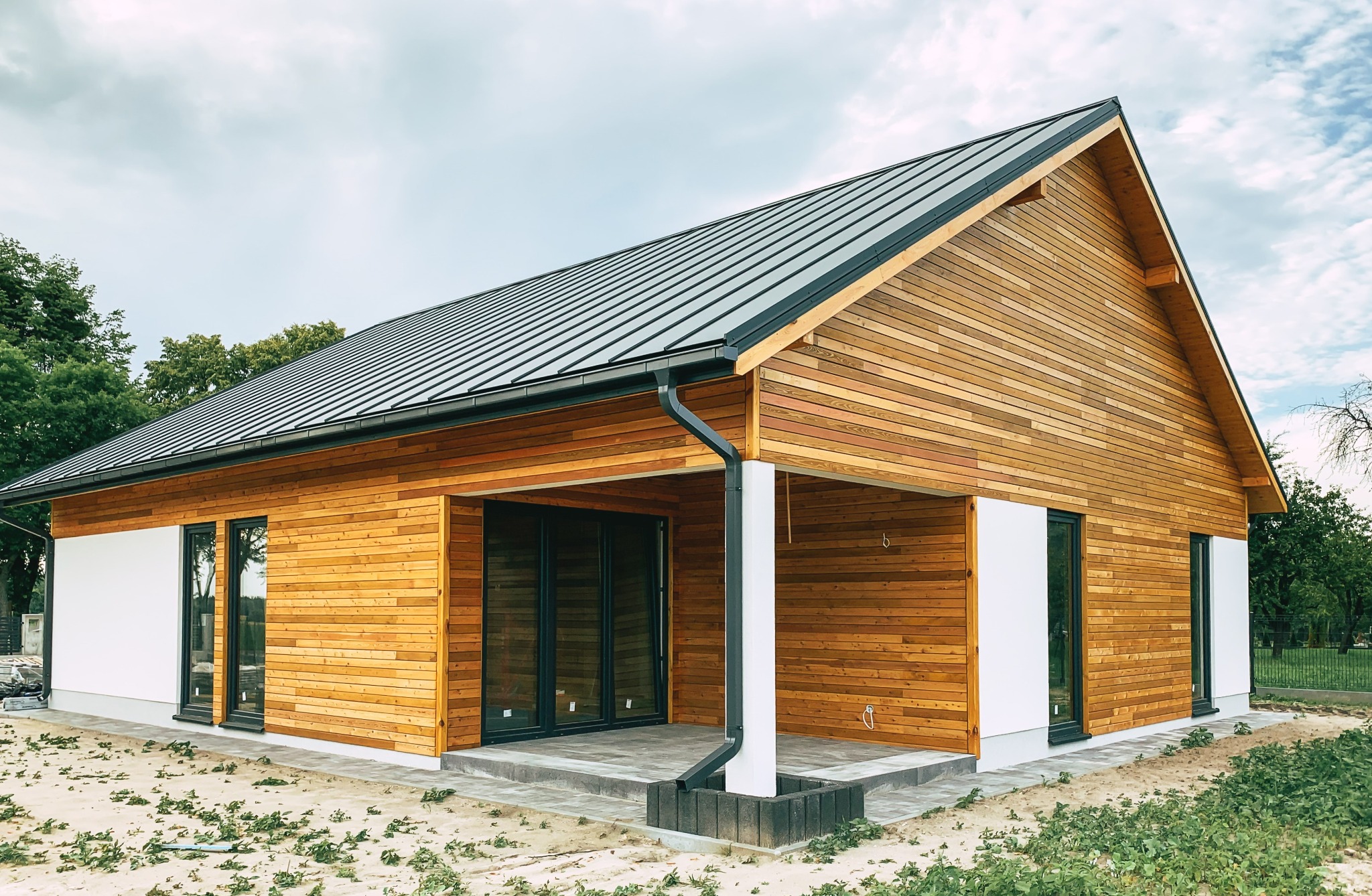 Nowoczesny dom jednorodzinny z drewnianą elewacją i metalowym dachem na tle pochmurnego nieba.