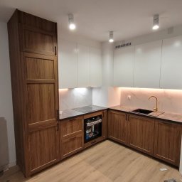 Perfekcyjnie Profesionalnie - Nowoczesna kuchnia z białymi górnymi szafkami i dolnymi szafkami z drewna, czarnym zlewem i złotą baterią, oświetleniem LED pod szafkami i trzema punktowymi lampami sufitowymi.