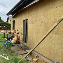 BudMex - Ocieplona ściana budynku z widoczną wełną mineralną, rusztowaniem i narzędziami. Etap prac przed nałożeniem warstwy wykończeniowej elewacji. Widok z zewnątrz.