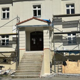 BudMex - Budynek w trakcie prac elewacyjnych. Widoczne rusztowania, świeżo pomalowana fasada i schody wejściowe. Prace wykończeniowe w toku, z widocznymi narzędziami i materiałami.