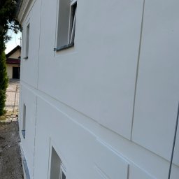 BudMex - Biała elewacja budynku po remoncie, widoczne okna i detale architektoniczne. Świeżo pomalowana fasada z elementami dekoracyjnymi.