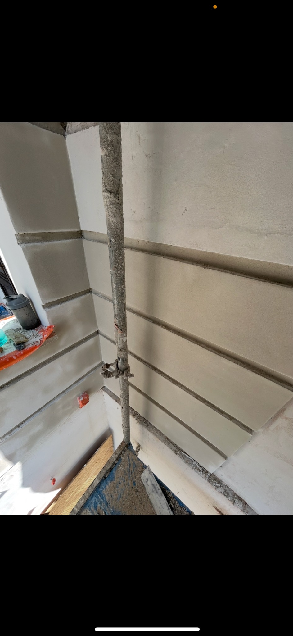 Ściana po szpachlowaniu z dekoracyjnymi pasami, widoczne rusztowanie i puszka farby. Detal wykończenia wnętrza z bliska, w neutralnej kolorystyce.