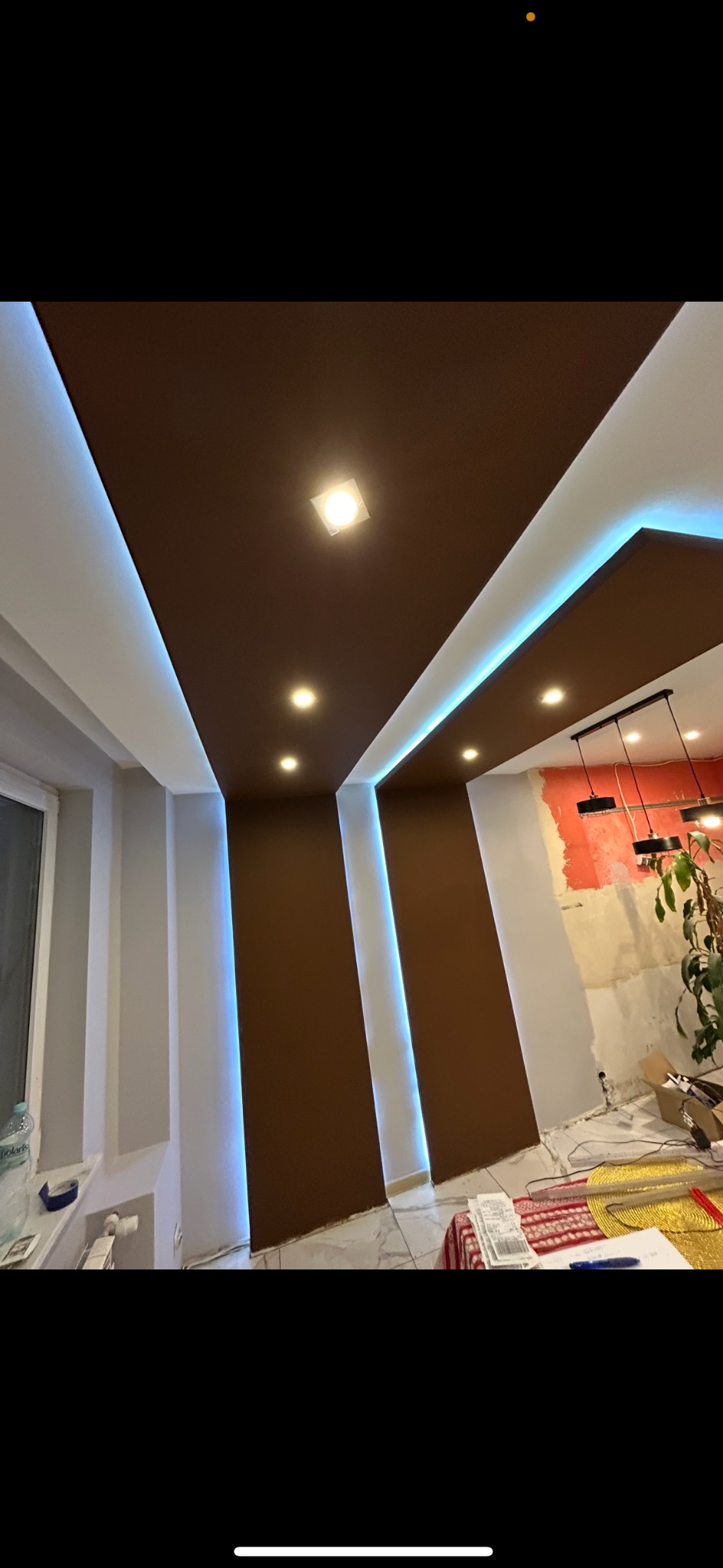 Nowoczesny sufit podwieszany z brązowymi panelami i oświetleniem LED w wyremontowanym wnętrzu. Widoczne lampy i fragment ściany w trakcie prac.