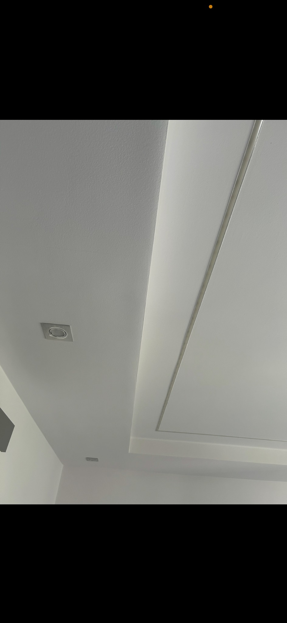 Biały sufit z dekoracyjnym wgłębieniem i oświetleniem punktowym. Minimalistyczny design, gładka powierzchnia, nowoczesne wykończenie wnętrza.