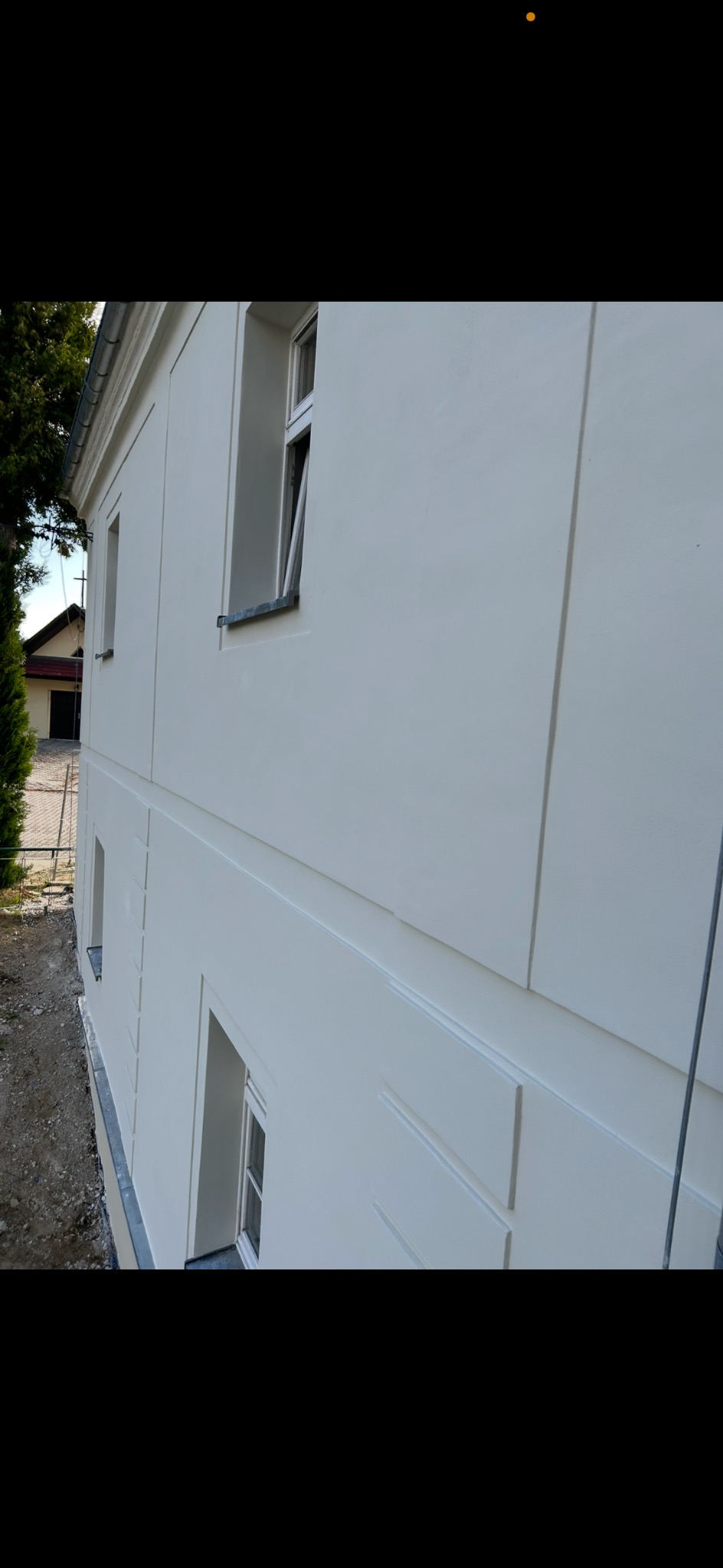 Biała elewacja budynku po remoncie, widoczne okna i detale architektoniczne. Świeżo pomalowana fasada z elementami dekoracyjnymi.