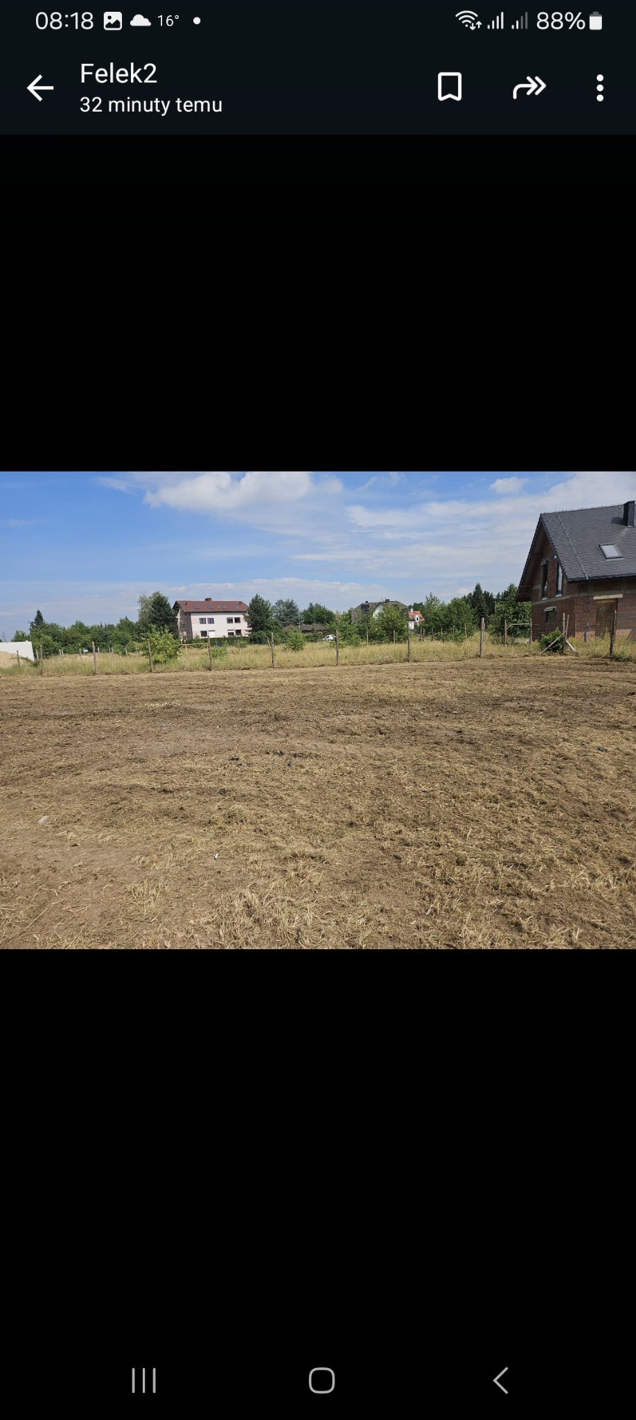 Przygotowany teren pod przyszły ogród, z widocznymi słupkami ogrodzenia, w tle budynki mieszkalne w letni dzień.