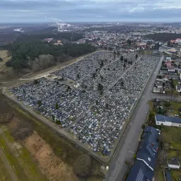 Panorama cmentarza z lotu ptaka, widok na miasto w tle, pochmurne niebo.