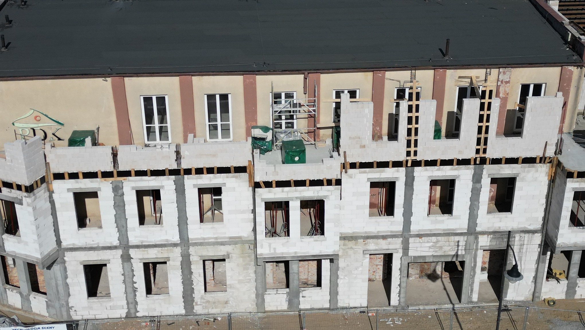 Wznoszenie murów budynku z betonu komórkowego, widok z góry na plac budowy z częściowo wykończonymi oknami i drzwiami, na górze widoczne rusztowania.