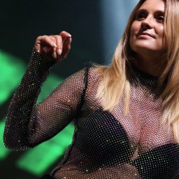 Krzysztof Raczyński - Fotografia - Portret kobiety z blond włosami, ubranej w błyszczącą, siatkową bluzkę na scenie z zielonym oświetleniem.