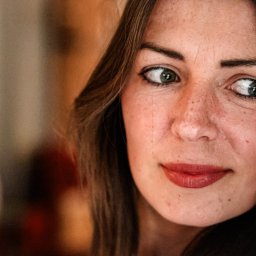 Krzysztof Raczyński - Fotografia - Portret kobiety z piegami, z zielonymi oczami i pomalowanymi ustami, spoglądającej w bok, z rozpuszczonymi brązowymi włosami.