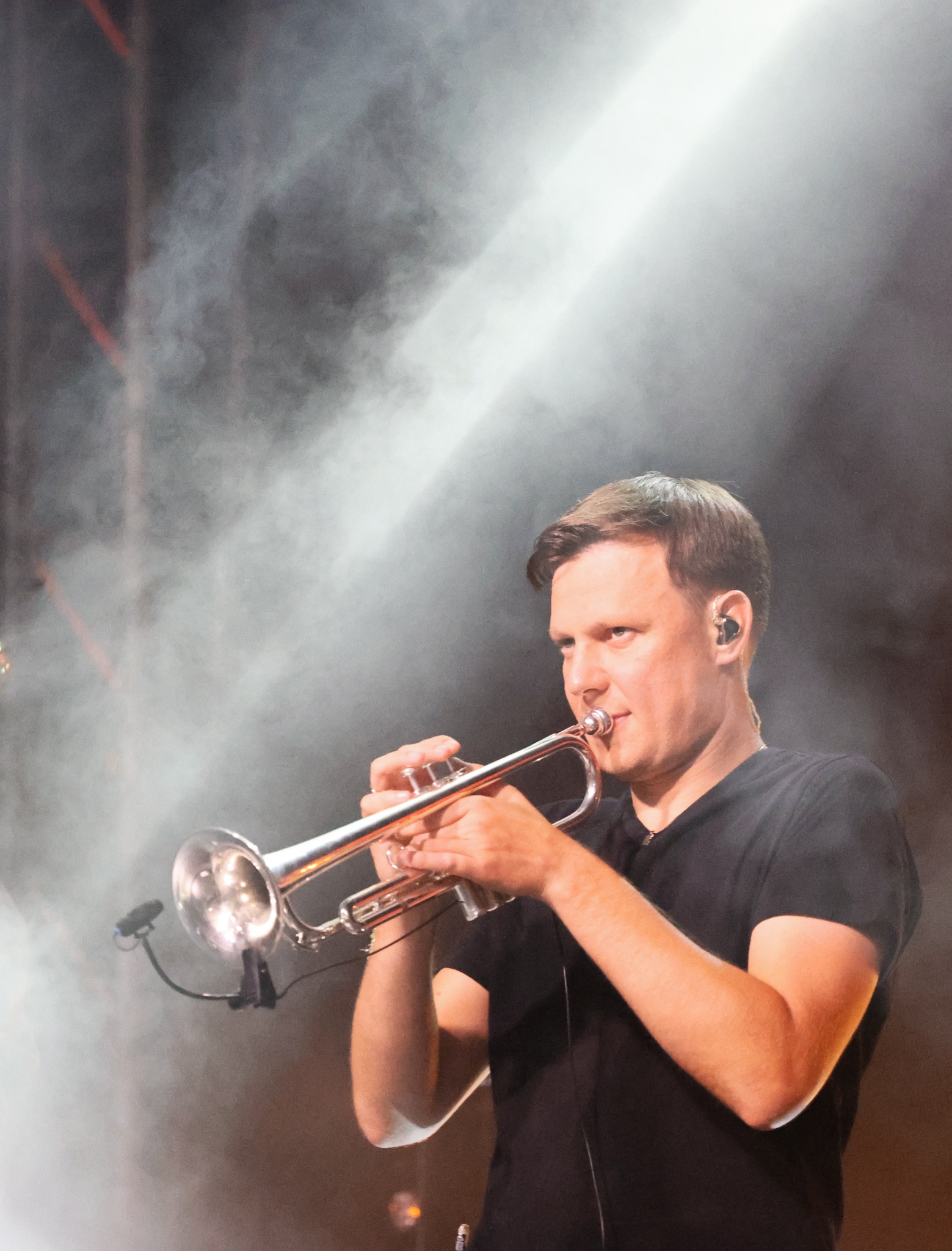 Muzyk grający na trąbce podczas występu na scenie w zadymionym oświetleniu punktowym.