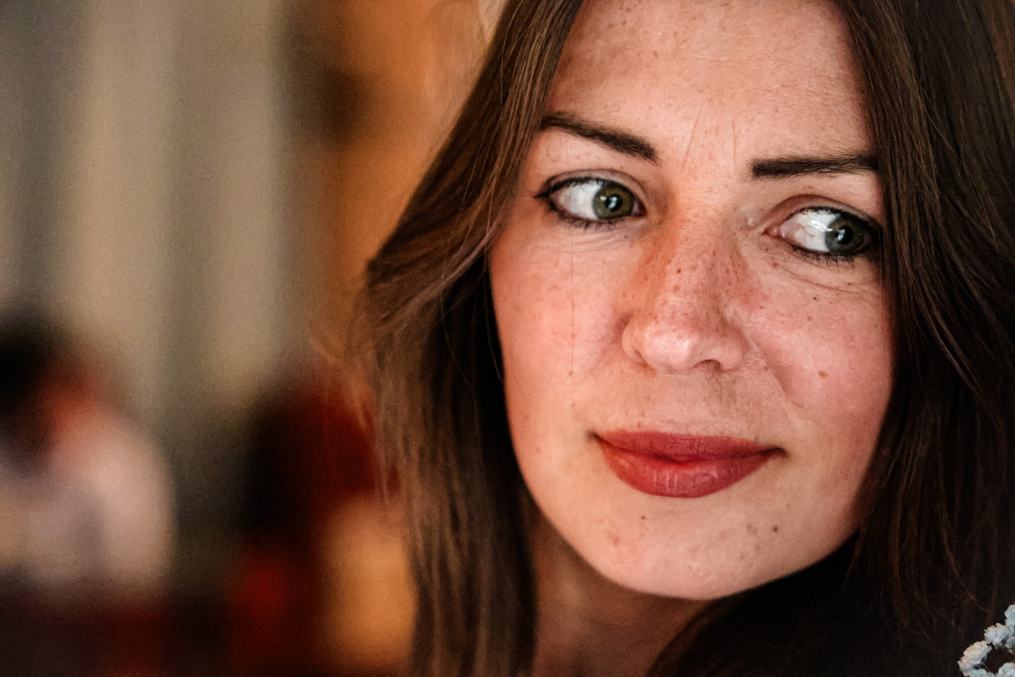 Portret kobiety z piegami, z zielonymi oczami i pomalowanymi ustami, spoglądającej w bok, z rozpuszczonymi brązowymi włosami.