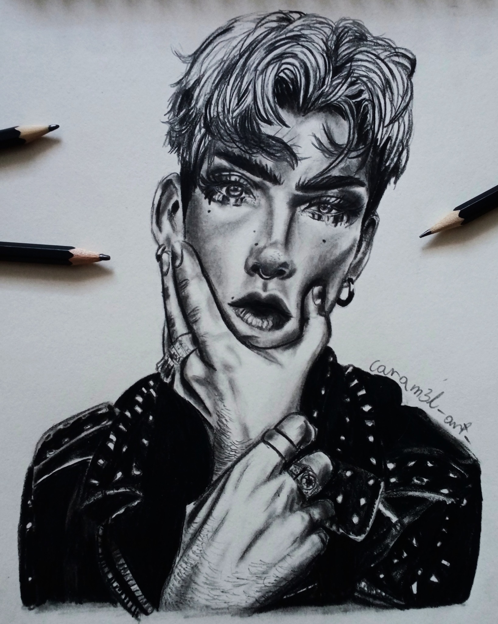 Czarno-biały portret osoby z piercingiem i mocnym makijażem, wykonany ołówkiem na papierze, z widocznymi ołówkami obok rysunku.