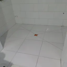 Białe, prostokątne płytki ułożone na ścianach i podłodze w łazience, z widocznym odpływem liniowym w podłodze i otworami na armaturę na ścianie.