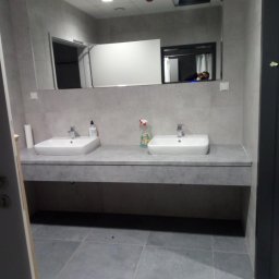 DREAM HOUSE Mateusz Zawisza - Szara łazienka z dwoma umywalkami, dużym lustrem i widoczną osobą odbijającą się w lustrze.