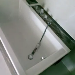 Biała wanna z zamontowaną chromowaną baterią, widoczny odpływ z metalowym łańcuszkiem, fragment marmurowego blatu.