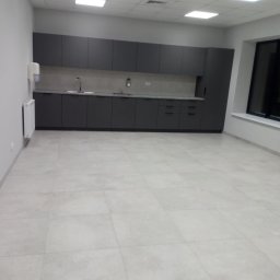 DREAM HOUSE Mateusz Zawisza - Nowoczesna, szara zabudowa kuchenna w biurowej przestrzeni z jasnymi płytkami podłogowymi i białymi ścianami, widoczny dozownik mydła i grzejnik.