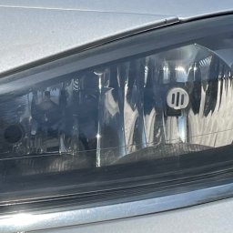 Shine - Reflektor samochodowy przed czyszczeniem z widocznymi smugami i zabrudzeniami, srebrny lakier karoserii.